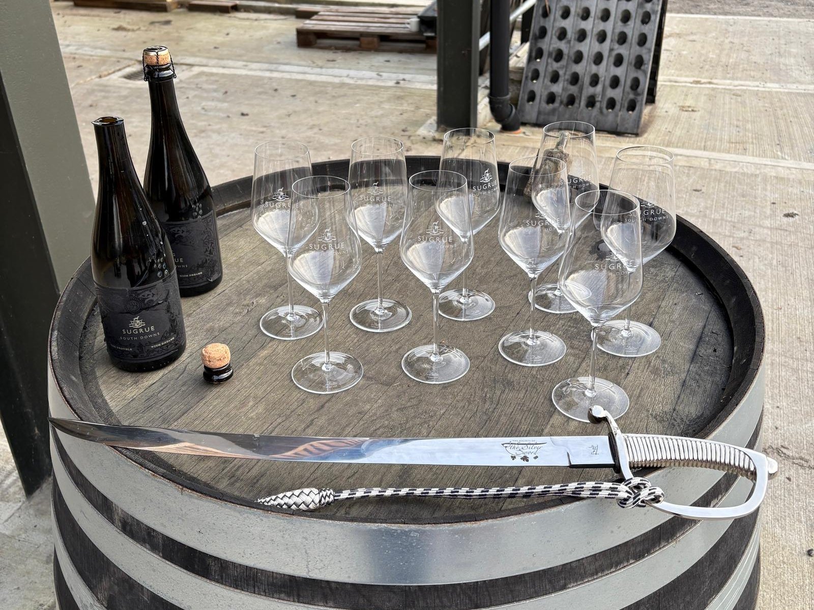 Silver Sword sword and Sugrue South Downs glasses and bottles on a wine barrel