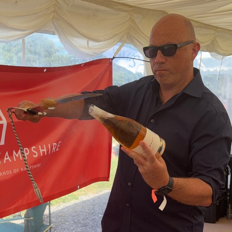 Man in sunglasses drawing a sabre along a bottle of rose